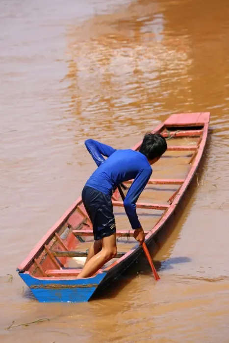  : Boy paddling a flooded sinking boat on the Mekong River in Luang Prabang, Laos