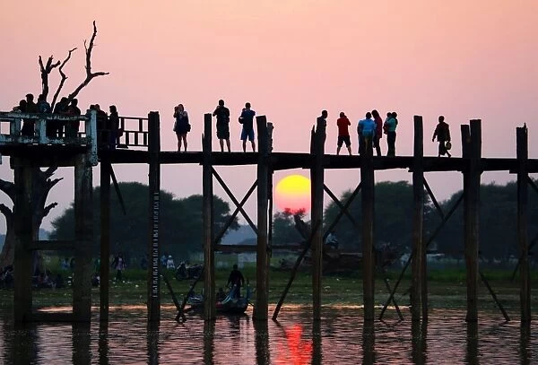 People crossing the U Bein Bridge across the Taungthaman Lake at sunset in Amarapura