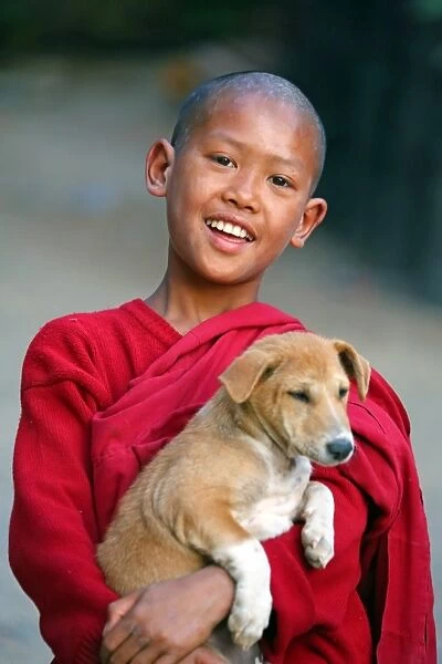 Portrait of a young Buddhist monk playing with a pet dog at a temple in Amarapura