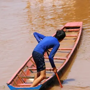 Boy paddling a flooded sinking boat on the Mekong River in Luang Prabang, Laos