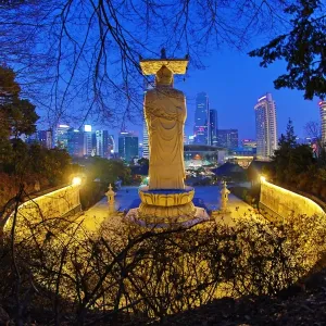Buddha statue and the city skyline at Bongeunsa Temple at sunset in Seoul, Korea