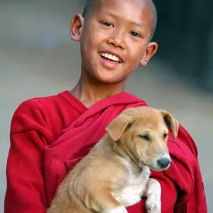 Portrait of a young Buddhist monk playing with a pet dog at a temple in Amarapura