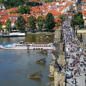 Tourists walking over the Charles Bridge over the Vltava River with a boat sailig