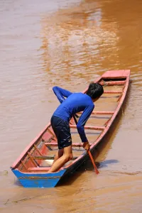 Luang Prabang, Laos: Boy paddling a flooded sinking boat on the Mekong River in Luang Prabang, Laos