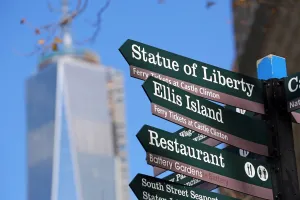 States: Direction signs to the Statue of Liberty and Ellis Island with One Trade Center ( 1 WTC ) in the background
