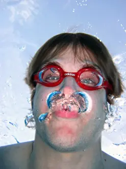 Swimmer: Man swimming underwater wearing goggles blowing bubbles