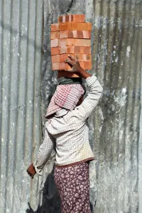 Site: Woman carrying bricks on her head on a building site in Amarapura, Mandalay, Myanmar